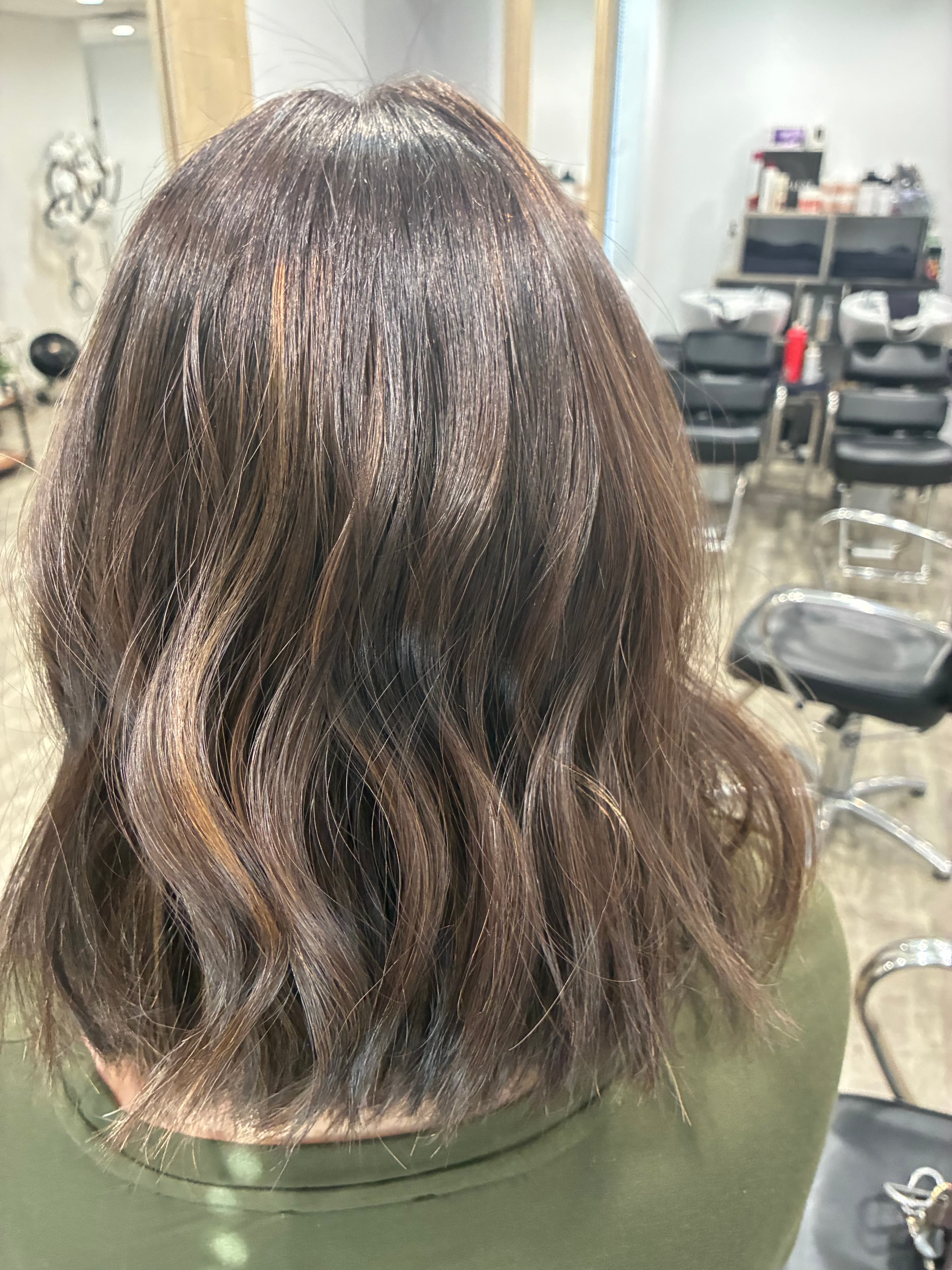 Shoulder-length wavy dark brown hair with subtle warm highlights, viewed from behind in a salon.