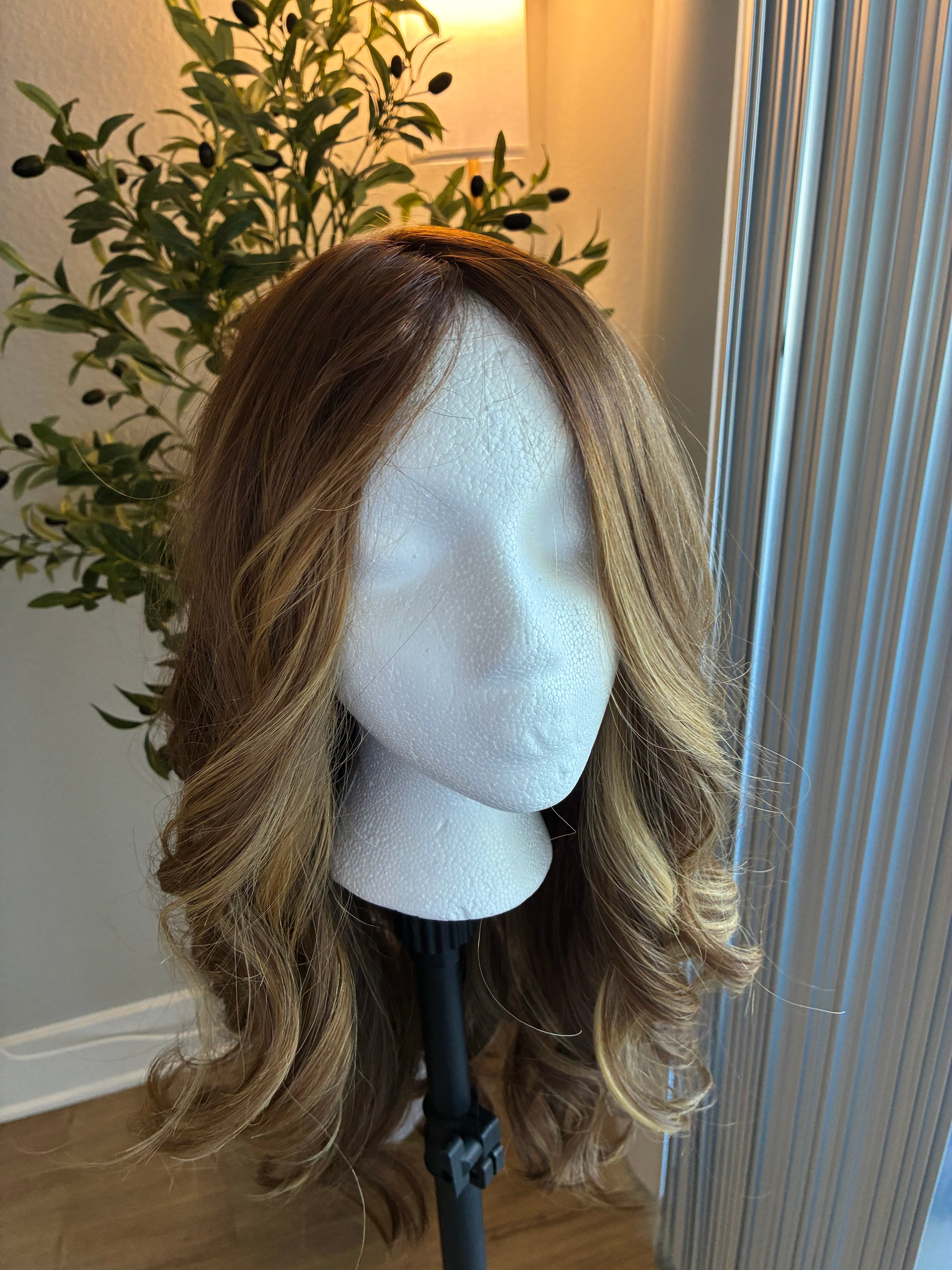Long wavy brunette wig with blonde highlights on a white styrofoam mannequin head stand.