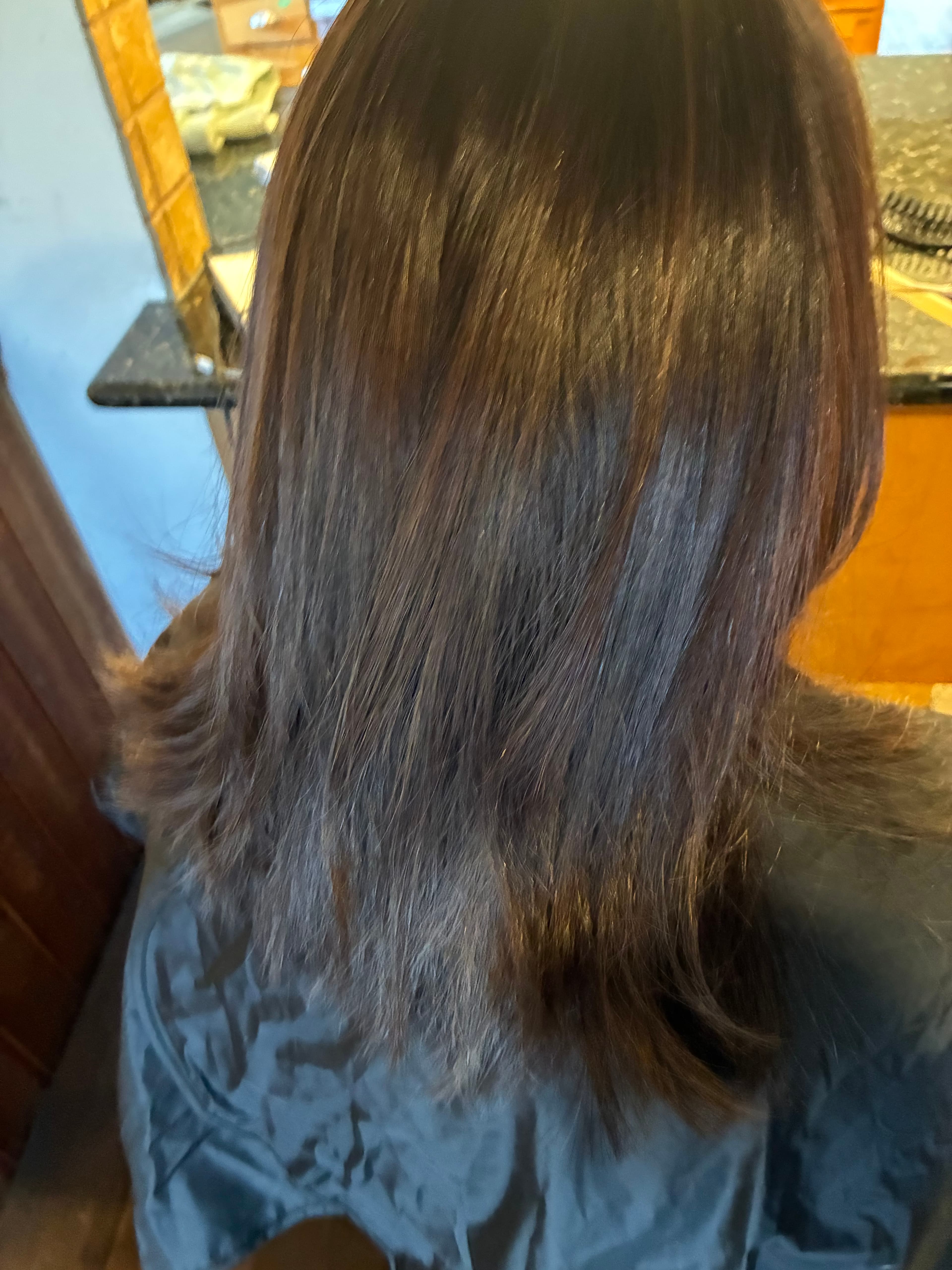 Back view of straight, shoulder-length dark brown hair draped over a black salon cape.