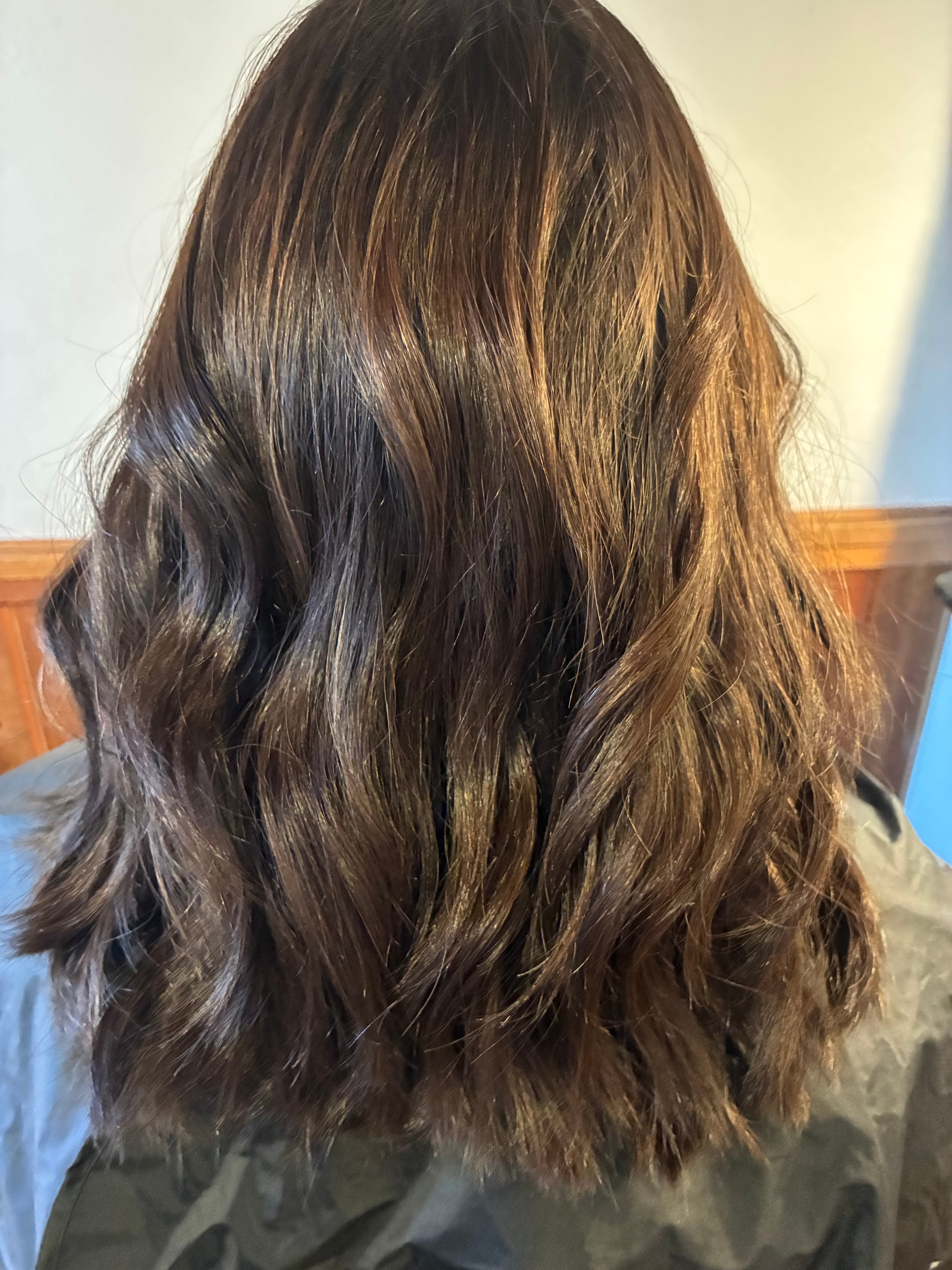 Shiny, shoulder-length dark brown hair styled in loose waves with subtle warm brown highlights.