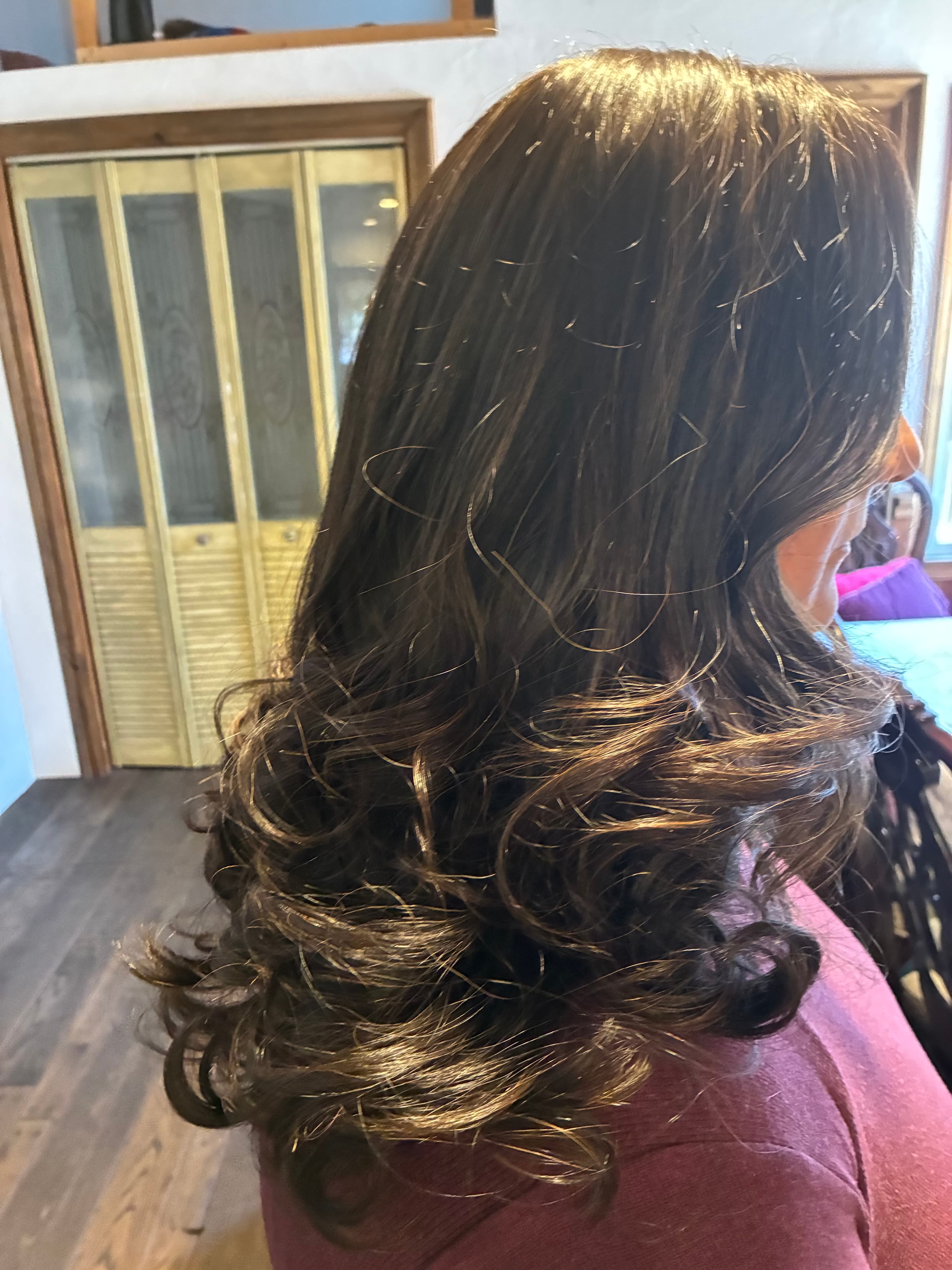Long, shiny brunette hair styled with voluminous, bouncy curls at the ends, viewed from the side.