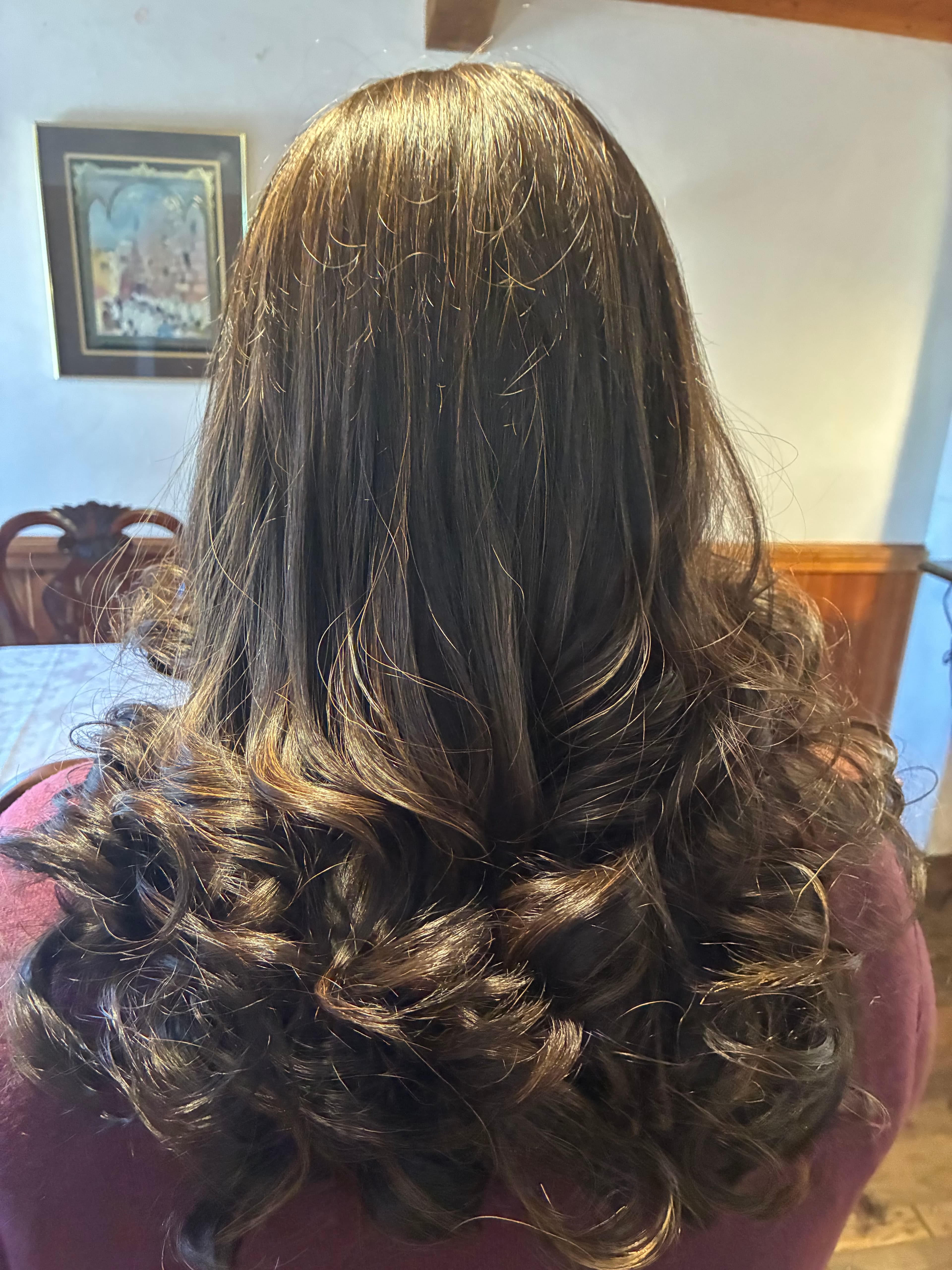 Long dark brown hair with straight roots and voluminous, bouncy curls at the ends.