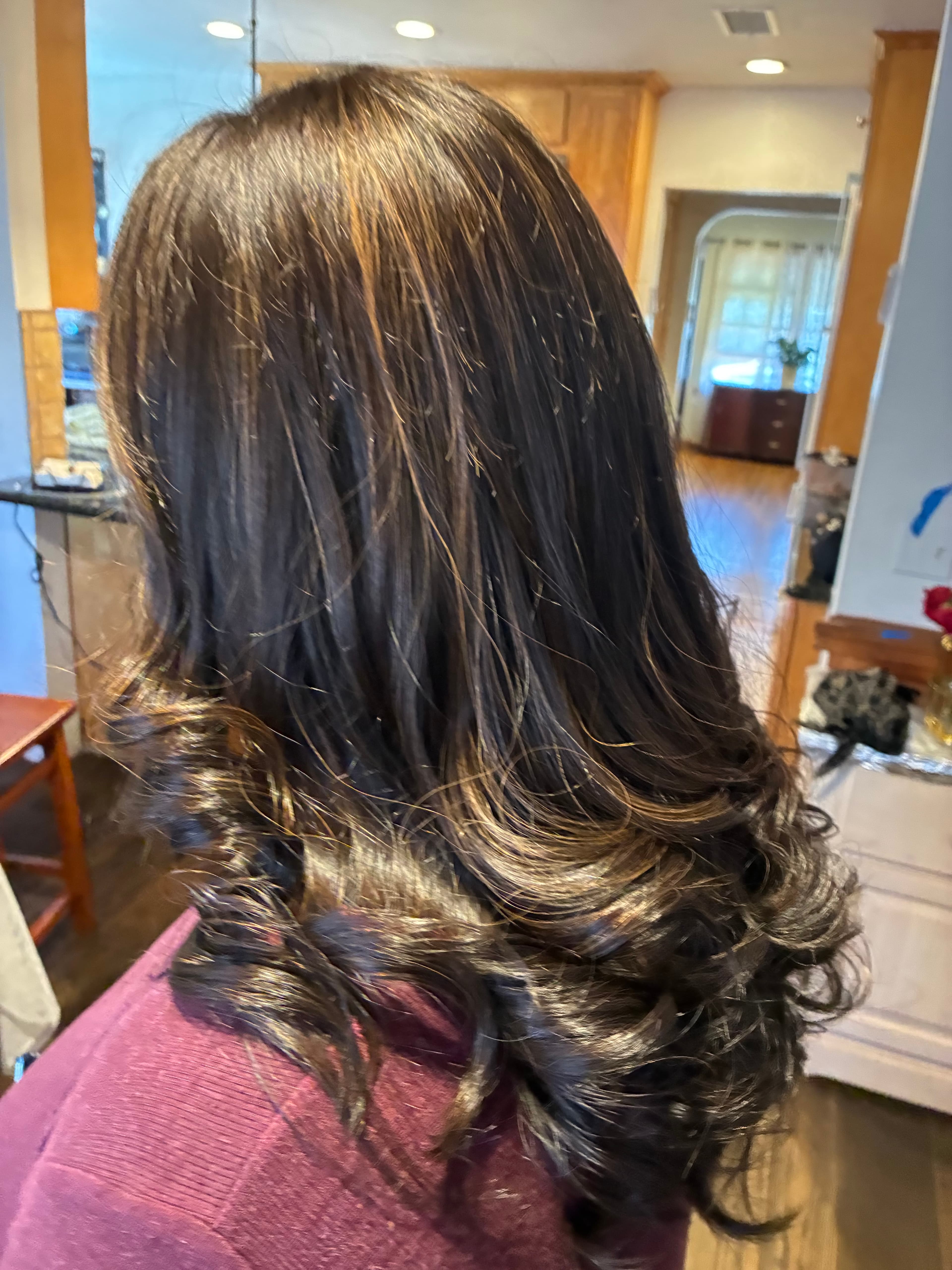 Long dark brown hair with warm highlights, styled with voluminous, bouncy curls at the ends.