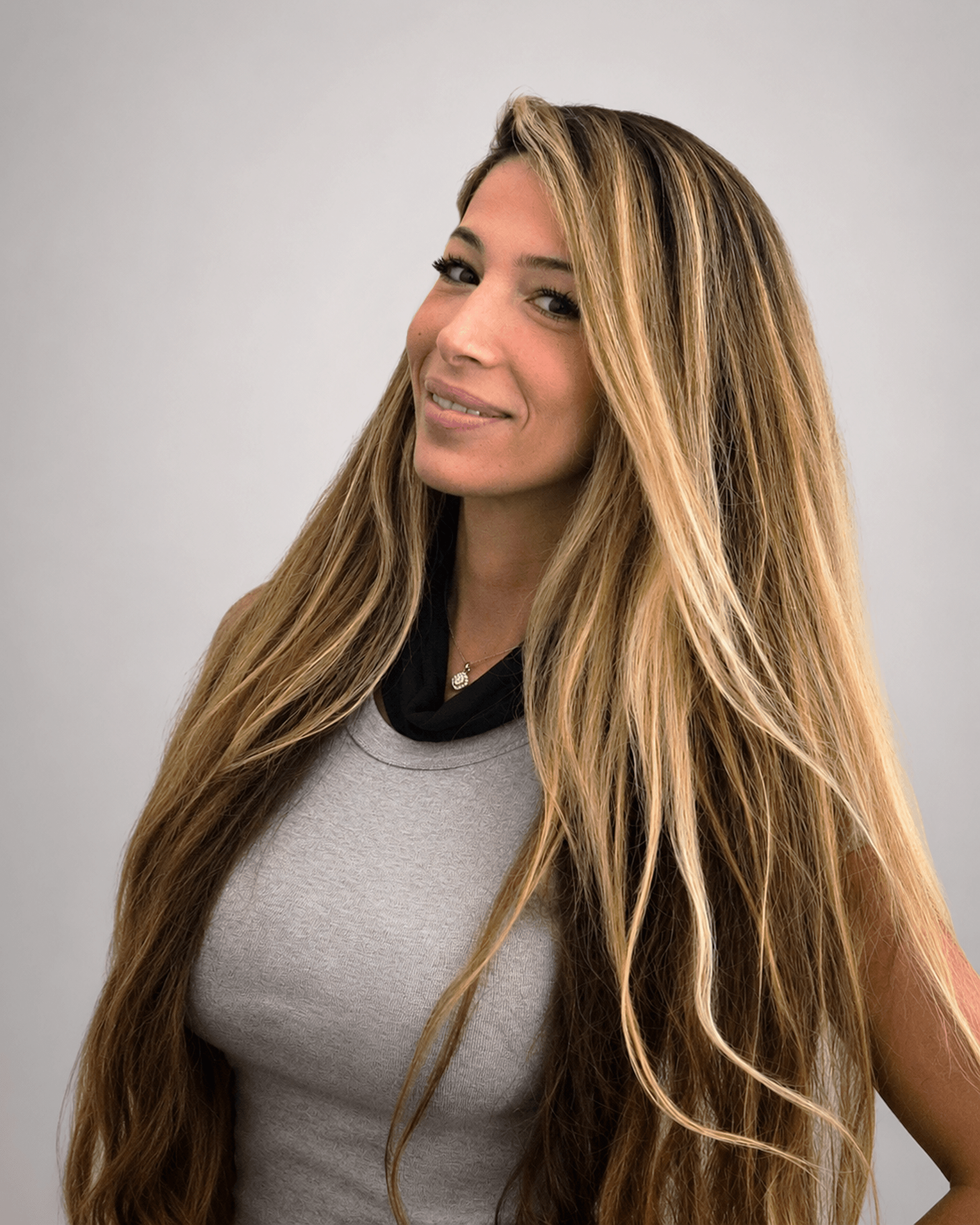 Smiling woman with very long, highlighted blonde hair wearing a grey top and black scarf.