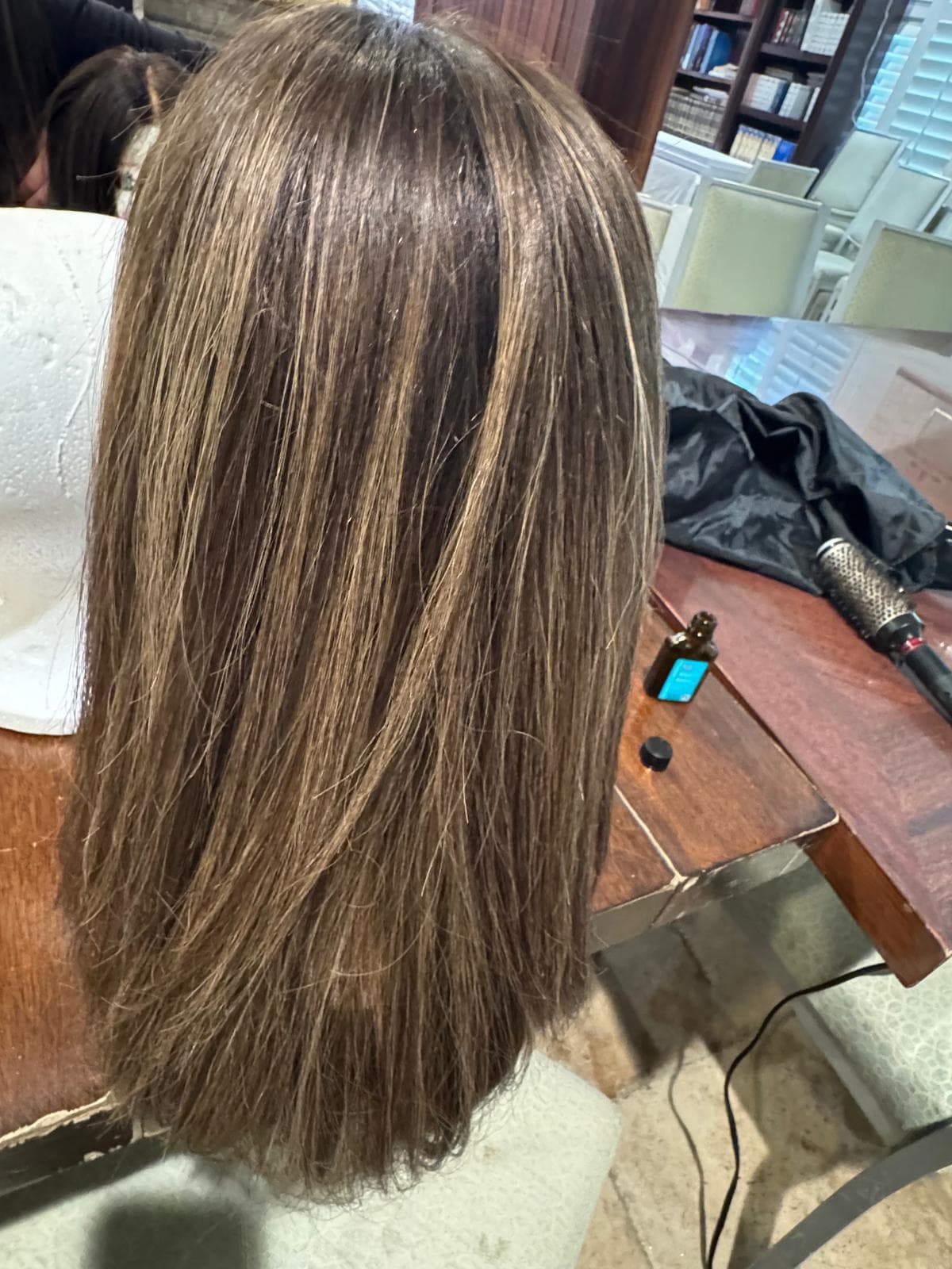 Long brown wig with blonde highlights on a mannequin head next to a hairbrush.